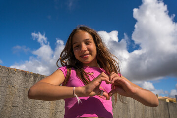 Smiling little tanned girl showing love sign and expressing happy emotions outdoors