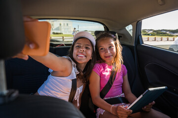 Wall Mural - Female best friends holding smartphone and making selfie while sitting at the car together