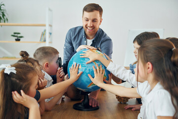 Learning geography by using Earth globe. Group of children students in class at school with teacher