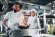 © standret - Igniting food in the frying pan. Professional chef preparing food in the kitchen