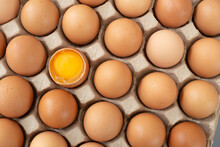 Flat Lay Close-up View Of Raw Chicken Eggs In Egg Paper Box. One Egg Cracked Showing The Yolk. Top View Natural Organic Egg. Fresh Chicken Eggs, Organic Eggs, Eggs For Food Ingredients, And Healthy Fo