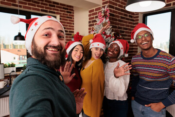 Wall Mural - Multiethnic group of people taking pictures with tree, celebrating festive season with christmas holiday decorations in business office. Colleagues taking photos with seasonal xmas ornaments.