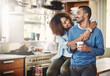 Leinwandbild Motiv Romantic loving couple, smiling and enjoying a cup of coffee in the morning together at home in their kitchen. Carefree wife hugging and bonding with husband while relaxing looking in love
