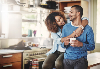 Poster - Romantic loving couple, smiling and enjoying a cup of coffee in the morning together at home in their kitchen. Carefree wife hugging and bonding with husband while relaxing looking in love