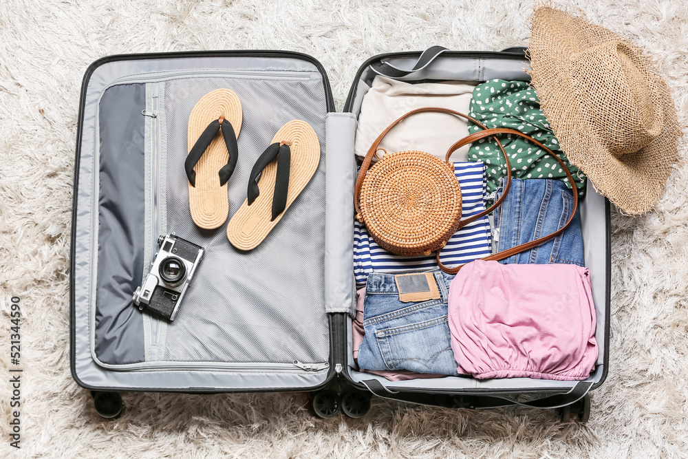 Opened suitcase with clothes and accessories for travelling on carpet