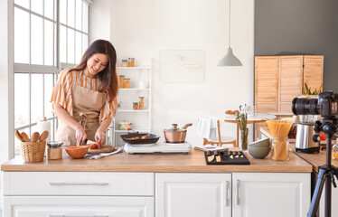 Poster - Young Asian woman cutting pumpkin while recording video class in kitchen