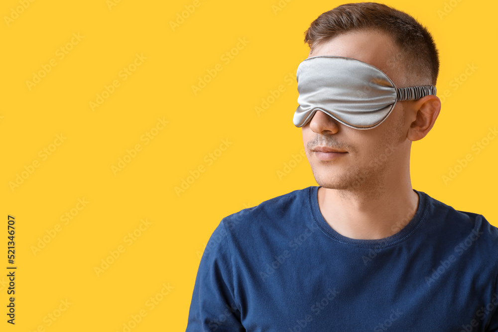 Young man with sleeping mask on yellow background