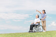 公園を散歩する介護士と車椅子の高齢者女性（青空）

