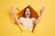 Portrait of excited beautiful woman wearing striped t shirt, showing big size with hands, looking at camera with amazed expression, looking through breakthrough of yellow background.