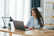 © standret - Freelance worker is sitting by table with laptop. Young beautiful woman is home alone in domestic room