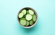 Leinwandbild Motiv Slices of fresh ripe cucumber in bowl on light blue background, top view