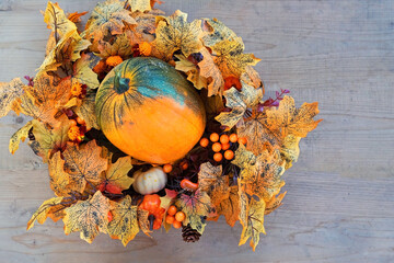 Wall Mural - ripe pumpkin and decorative bright autumn wreath on wooden background. fall season concept. Symbol of Thanksgiving day, Halloween, Autumn harvest. top view