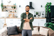 © Kateryna - Portrait of a handsome positive modern indian or arabian guy, in casual stylish clothes, standing at home in the living room on the background of the kitchen, with crossed arms, looks at camera, smile