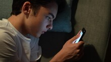 Tired Teenager Boy Text Messaging On Phone, Then Yawning. Closeup Of Handsome Guy Laying On Couch At Night