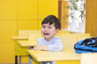 © Alexandra - preschooler boy is crying sitting on school desk. angry unhappy sad upset kid don't want to go back to school, refuse.tears on cheeks one hand cover eye.backpack on table.education first day alone