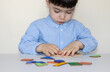 © Alexandra - serious face baby boy playing tangram puzzle on school desk white table.isolated kid back to school kindergarten concept.high iq child smart kid.classroom home activities intellectual development