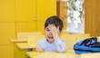 © Alexandra - preschooler boy is crying sitting on school desk. angry unhappy sad upset kid don't want to go back to school, refuse.tears on cheeks one hand cover eye.backpack on table.education first day alone