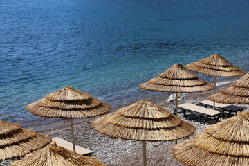 Empty pebble beach with wicker parasols and lounge chairs. Picturesque view to sea with blue water, summer resort