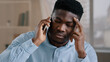© Yuliia - African man businessman american male employee worker answer incoming call talking on phone in home office disappointed frustrated young guy receiving bad news failed transaction negative information