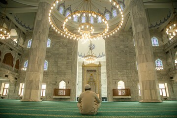 Man in a traditional Islamic outfit praying inside a mosque.