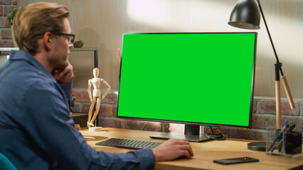 Poster - Young Handsome Man Working from Home on Desktop Computer with Green Screen Mock Up Display. Creative Male Checking Social Media, Browsing Internet. Living Room in Bright Loft Apartment.