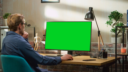 Poster - Young Handsome Man Working from Home on Desktop Computer with Green Screen Mock Up Display. Creative Male Checking Social Media, Browsing Internet. Living Room in Bright Loft Apartment.