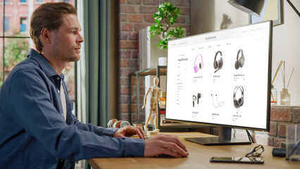 At Home Office: Man Using Desktop Computer, Online Shopping for Electronics, Wireless Hi-Fi Headphones. e-Commerce Concept of Purchasing, Buying, Ordering Tech Devices on Website. Over Shoulder View