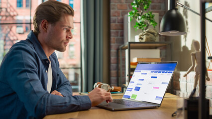 Poster - Young Handsome Man Working on Freelance from Home on Laptop Computer with Office Software on Display. Creative Male Checking Timetable, Planning Meetings. Living Room in Loft City Apartment.