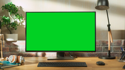Poster - Desktop Personal Computer Monitor Standing on a Table with a Green Screen Chromakey Mock Up Display. Cozy Empty Loft Apartment with a Lamp, Notebooks and Headphones on the Table.