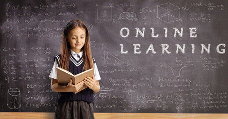 Canvas Print - Schoolgirl reading a book in front of a chalkboard with text online learning