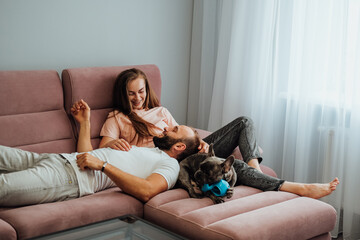 Adult Couple Having Leisure with French Bulldog at Home, Cheerful Woman and Man Relaxing on Pink Sofa with Pet