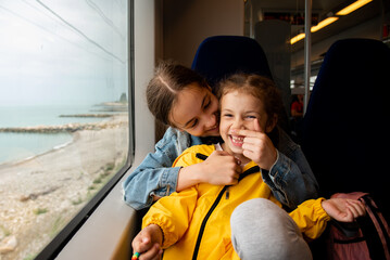 Two sister girls look out the window of a train at the sea.The girls are talking and having fun. Journey. Reflection. Vacation. Summer. Family vacation.