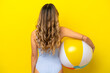 © luismolinero - Young woman holding beach ball isolated on yellow background in back position