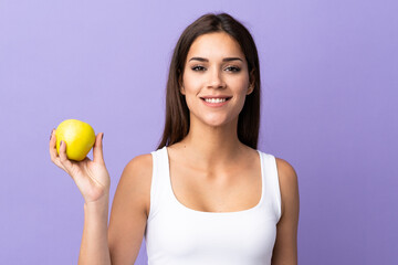 Sticker - Young caucasian woman isolated on purple background with an apple and happy