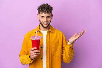 Canvas Print - Young blonde man holding soda isolated on purple background extending hands to the side for inviting to come