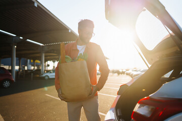 Wall Mural - Young man with shopping bag full of vegetables near the car. Healthy lifestyle.