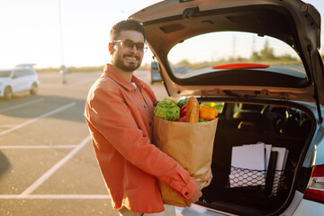 Wall Mural - Young man with shopping bag full of vegetables near the car. Healthy lifestyle.