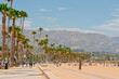 Santa Barbara beach promenade with walking people, sandy beach, and mountains and cloudy sky on background