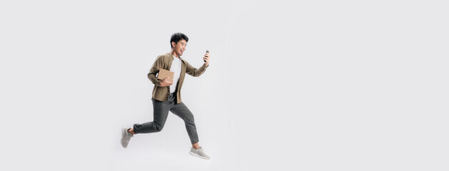 Wall Mural - Full length handsome Asian man holding box and use smartphone he is run and jumping in air on banner white background. Young male happy excited and using mobile phone with shopping online concept.