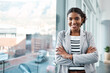 Young, confident and ambitious business woman or corporate professional standing arms crossed by an office window in the city. Portrait of a happy female ready for success and looking positive