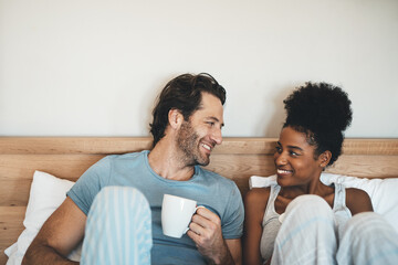 Poster - Happy young interracial couple having a cup of coffee on a bed in the morning at home. Romantic people in love, smiling in the bedroom with a warm beverage with loving man and woman in happiness.