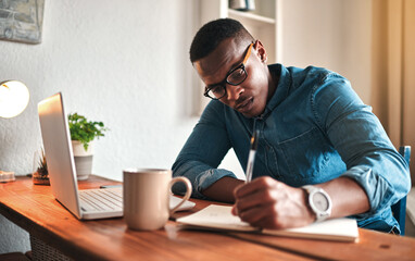 Poster - African american entrepreneur writing in a notebook and planning a project strategy. Young man remote working from home with a laptop at his startup business while scheduling appointments in a book