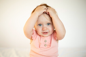 Portrait of a charming funny red-haired baby girl with blue eyes and a birthmark on her cheek. Hemangioma. Light background. Lifestyle