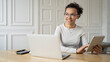 © muse studio - A female student with glasses smiles works in the office uses a laptop to surf the Internet