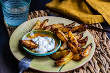 Close-up Of Baked Potato Wedges With Sour Cream, Garlic And Dill Dip With A Glass Of Water