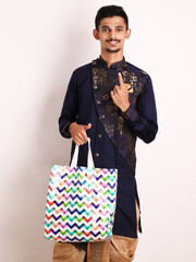 Wall Mural - Confident Indian young boy holding shopping bag and Showing Number One while wearing traditional ethnic wear. One Percent Off Concept. Diwali Shopping. Isolated over white background.