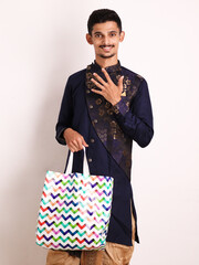 Wall Mural - Confident Indian young boy holding shopping bag and Showing Number Five while wearing traditional ethnic wear. Five Percent Off Concept. Diwali Shopping. Isolated over white background.