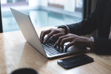 Sticker - Businessman working on laptop computer with mobile phone on wooden table at modern office. Business man hands typing on laptop keyboard, online working