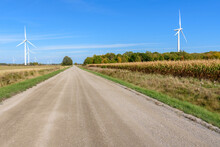 Wind Turbines Along A Straight Unpaved Country Road Under Blue Sky In Autumn
