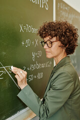 young confident teacher in eyeglasses and smart casualwear drawing angle on blackboard with chalk wh